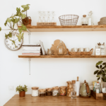 Uma mesa cheia de utensílios de cozinha e plantinhas. Acima, duas prateleiras com itens decorativos.